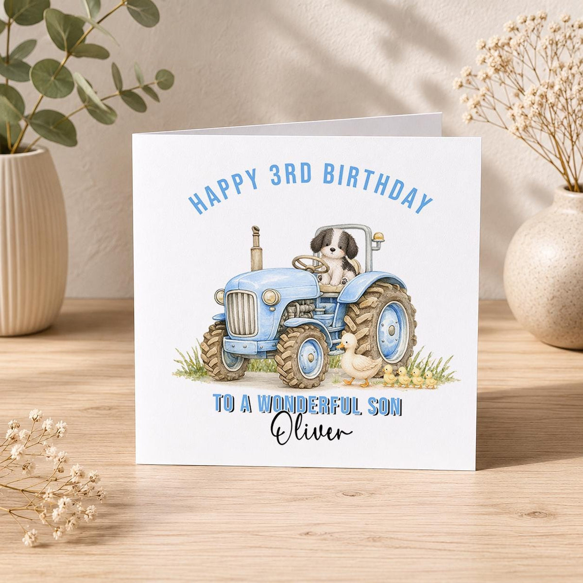 Square personalised birthday card showing a blue tractor driven by a cartoon puppy, with a duck and ducklings alongside, reading Happy 3rd Birthday to a wonderful Son Oliver.