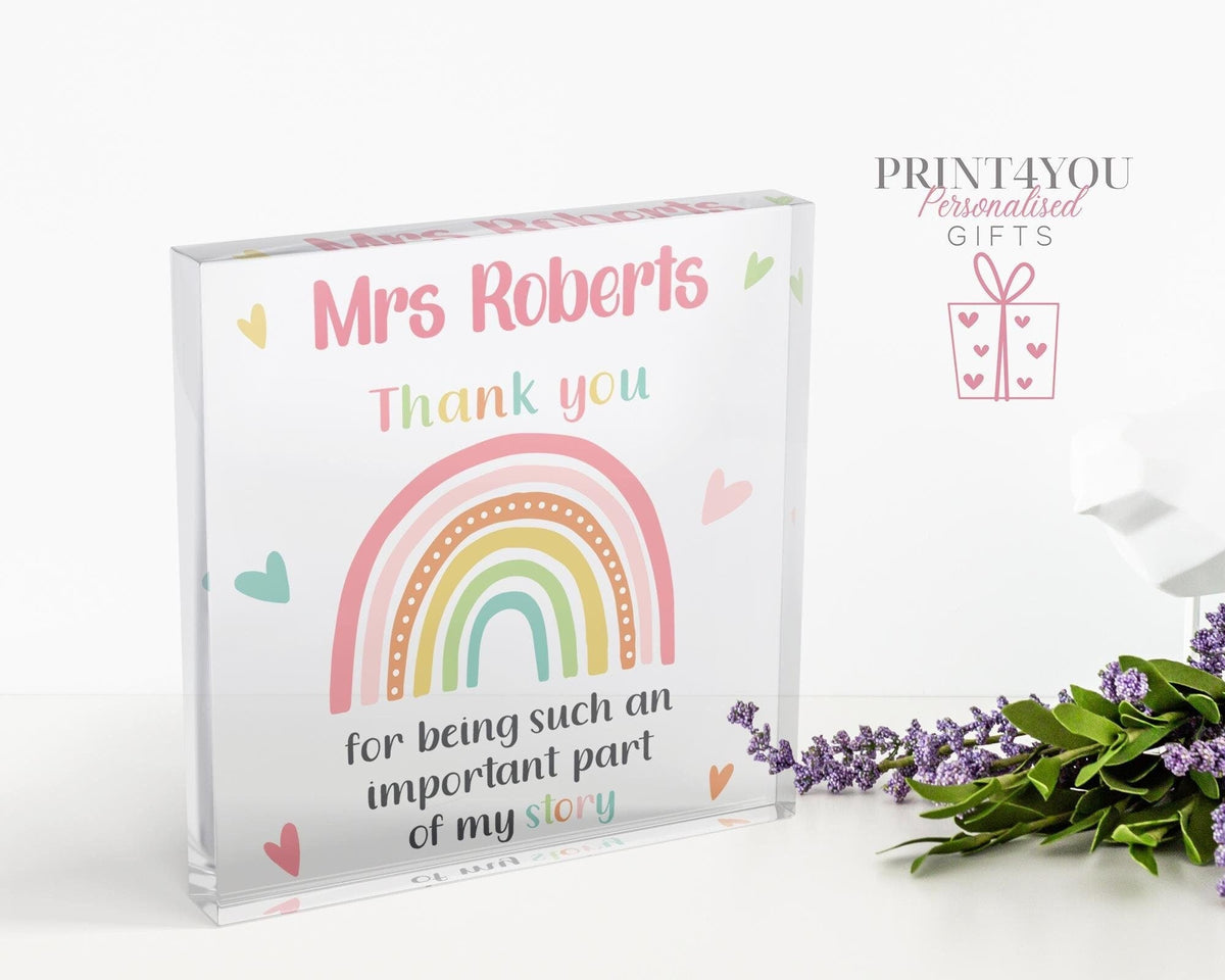 Clear freestanding acrylic block printed with 'Mrs Roberts, Thank you for being such an important part of my story' beside a pastel rainbow design, standing on a white desk.