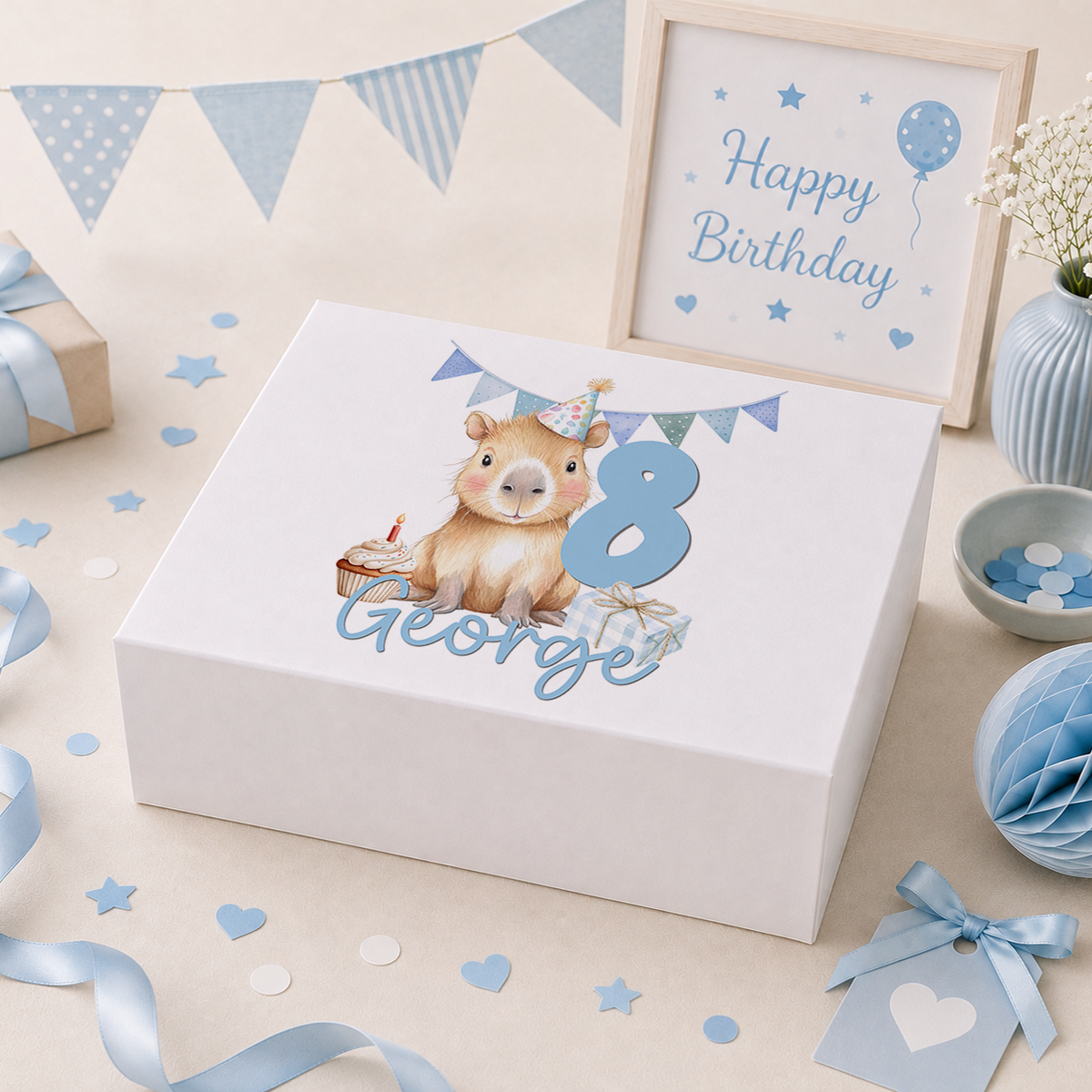 Personalised white keepsake box with magnetic lid, showing a party-hatted capybara beside a cupcake and a wrapped gift, a pastel blue number 8 and the name George, styled with birthday bunting, balloons and confetti props