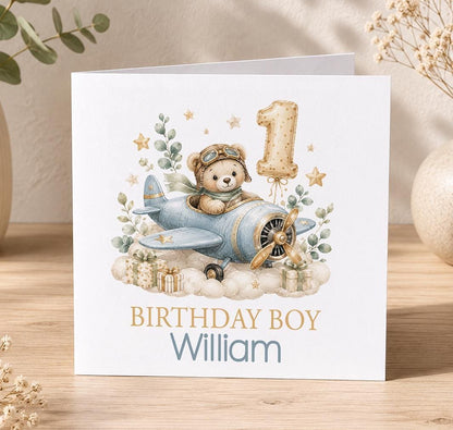 Personalised teddy aeroplane 1st birthday card – teddy flying a blue plane with a gold number 1 balloon, Birthday Boy William