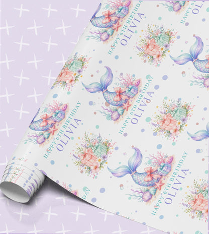 Personalised mermaid birthday wrapping paper with watercolour mermaid tails, coral, starfish and treasure chests, printed with Happy 6th Birthday and the name Olivia on a lilac sparkle background