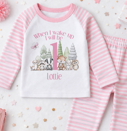 A pink and white striped onesie with a cartoon image of woodland animals and the text "When I wake up I will be 1 Lottie" printed on it.