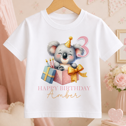 White kids t-shirt with a cartoon koala wearing a birthday hat and holding a gift box, personalised with a birthday message and name