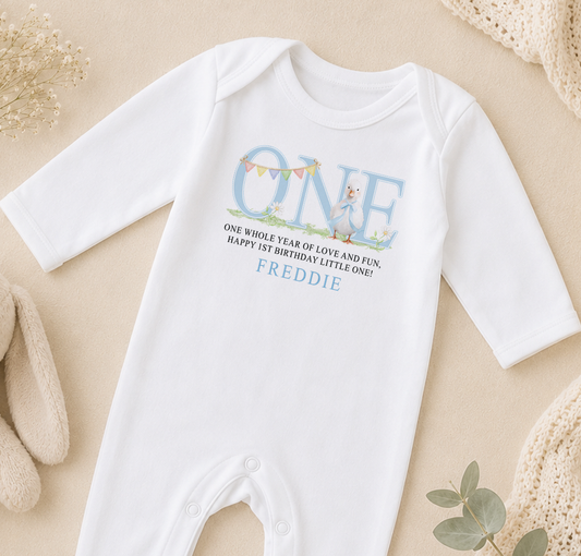 White baby onesie printed with a blue duckling, bunting and a personalised first birthday message.
