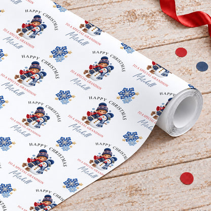 Roll of personalised grandson Christmas wrapping paper with a boy hugging a snowman, blue snowflakes and gold stars