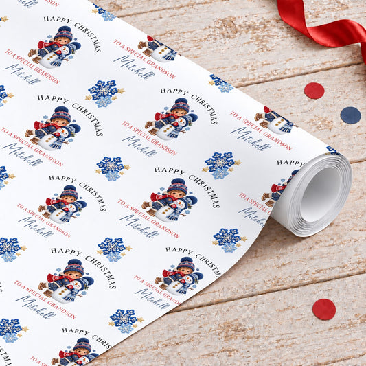Roll of personalised grandson Christmas wrapping paper with a boy hugging a snowman, blue snowflakes and gold stars