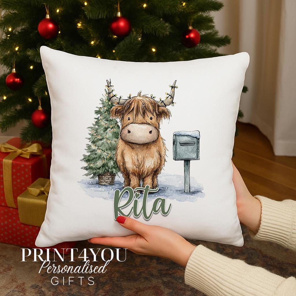 Square cushion personalised with a name, printed with a Highland cow in a festive scene with fairy lights, snowy tree and postbox