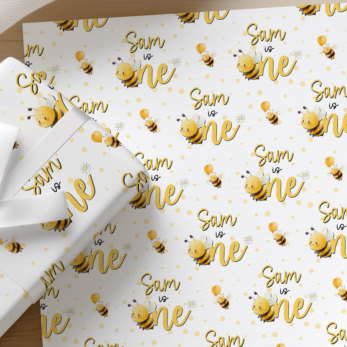 Flat lay of personalised bee 1st birthday wrapping paper with a name printed across the sheet