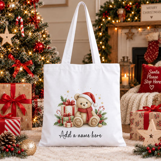 White cotton tote bag printed with a teddy bear in a Santa hat and scarf among red Christmas presents and candy canes, with a personalised name below
