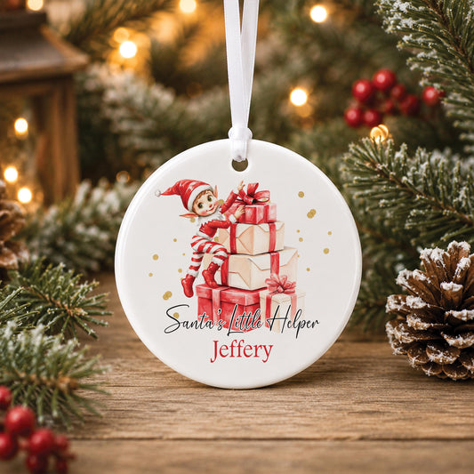 Personalised white ceramic Christmas bauble featuring a watercolour Christmas elf sitting on stacked presents, Santa's Little Helper wording and a child's name