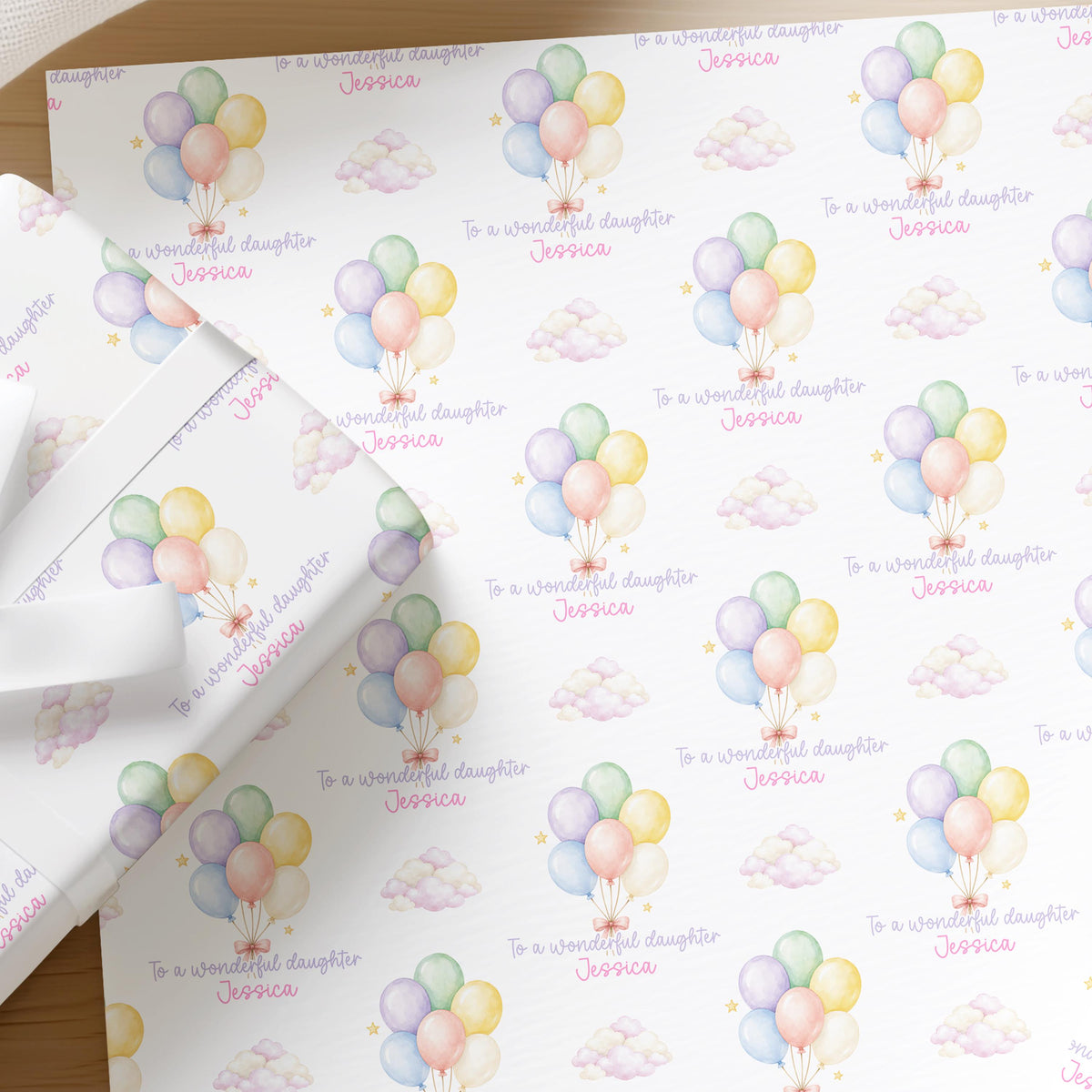 Flat lay of personalised daughter wrapping paper featuring pastel balloons and a name printed across the sheet