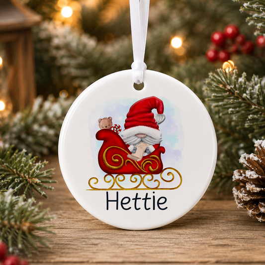 A white ceramic ornament with a red Santa Claus sled and a teddy bear, hanging on a Christmas tree.
