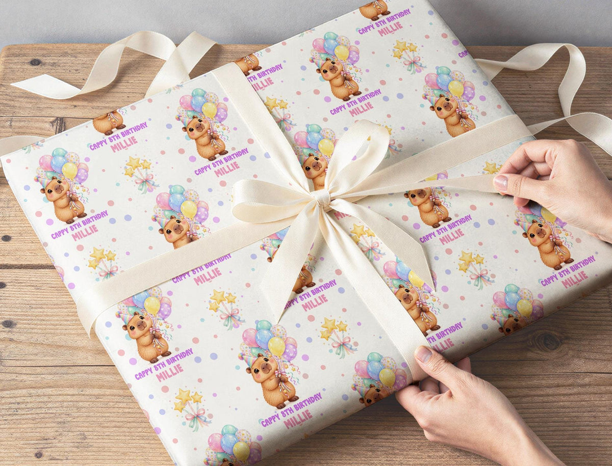 Gift wrapped in personalised capybara and balloons birthday wrapping paper, tied with a cream ribbon on a wooden table