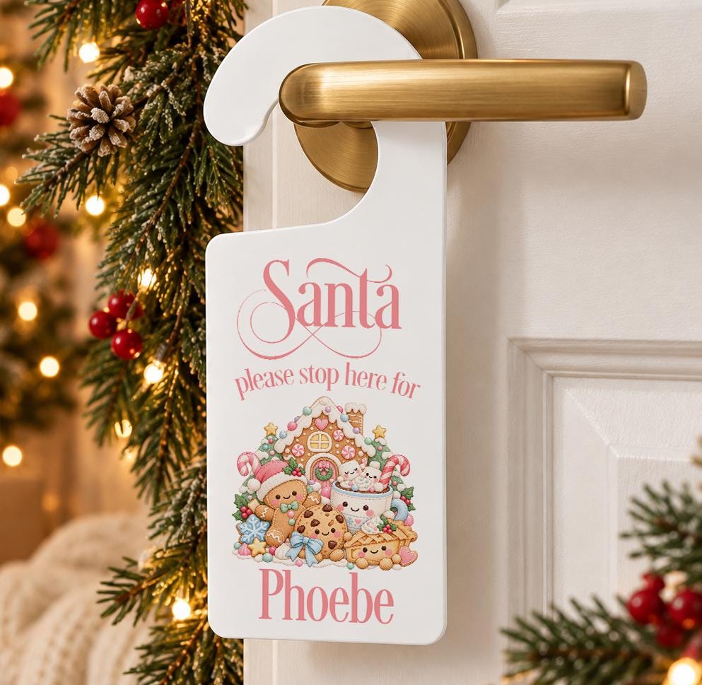 Personalised pink Santa please stop here door hanger with a frosted gingerbread house and child’s name, hanging on a door handle