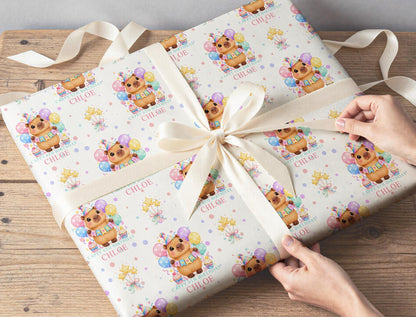 Gift wrapped in personalised capybara and balloons birthday paper, tied with cream ribbon on a wooden table