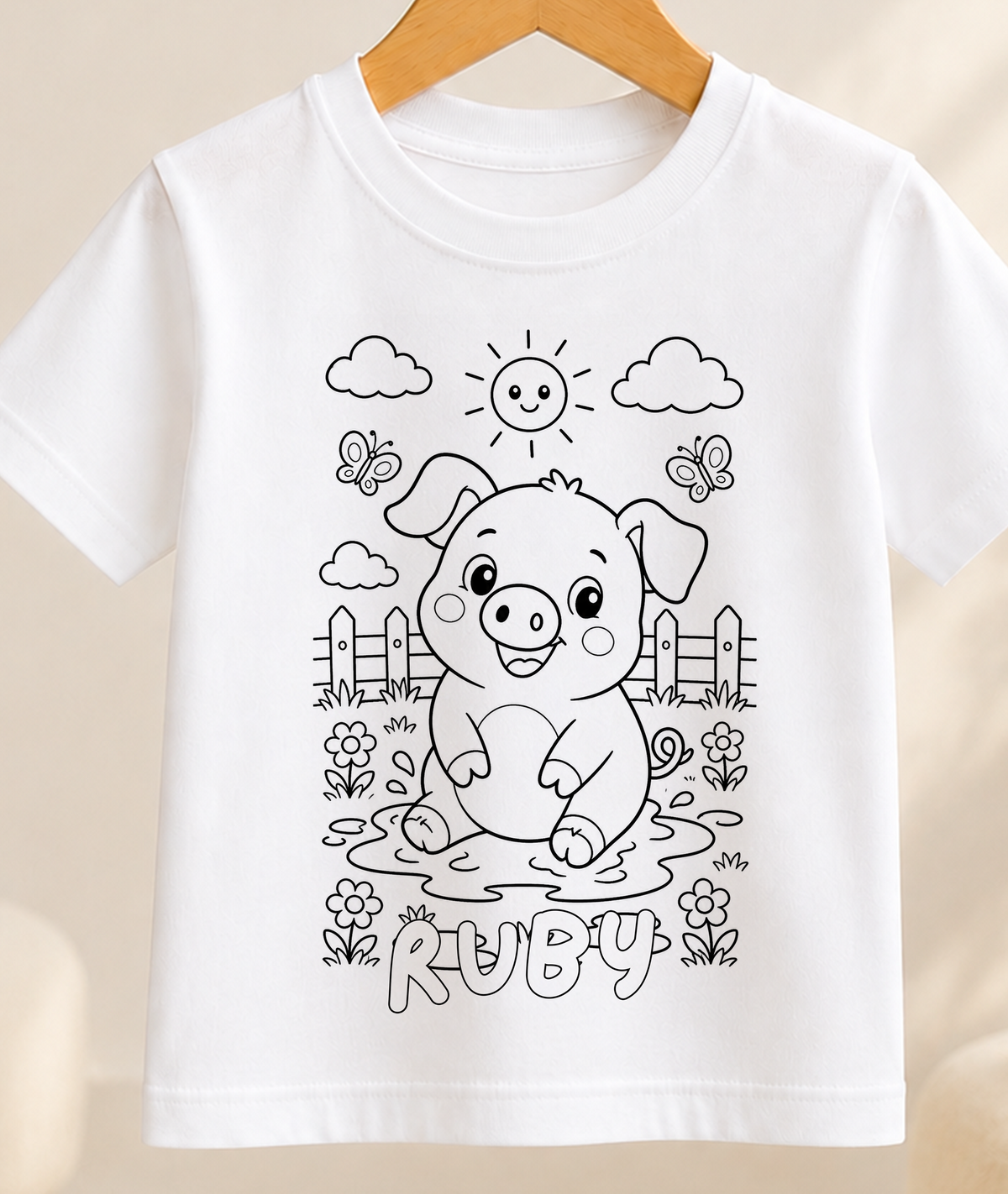 Colour-in kids t-shirt with a black-and-white line art pig in a farmyard scene, personalised with a name in bubble letters