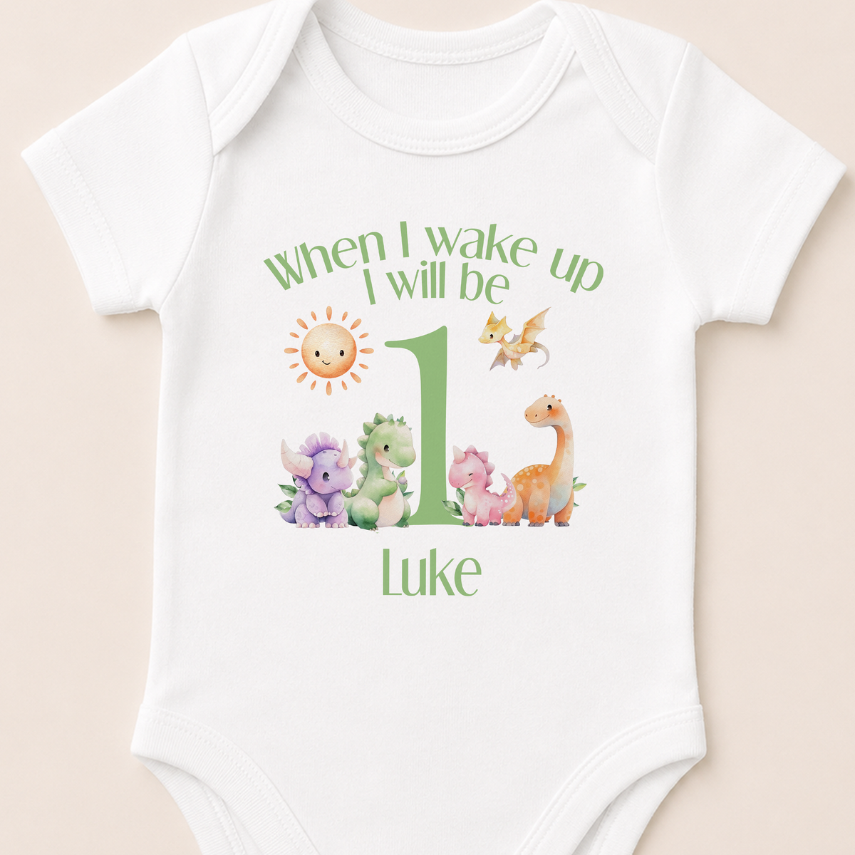 White baby sleepsuit personalised with a green dinosaur design and the message 'When I Wake Up I Will Be One'.