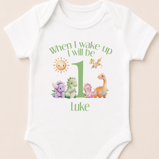 White baby sleepsuit personalised with a green dinosaur design and the message 'When I Wake Up I Will Be One'.