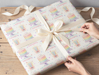 Gift wrapped in personalised pastel rainbow cake and candles birthday wrapping paper, tied with a cream ribbon on a wooden table