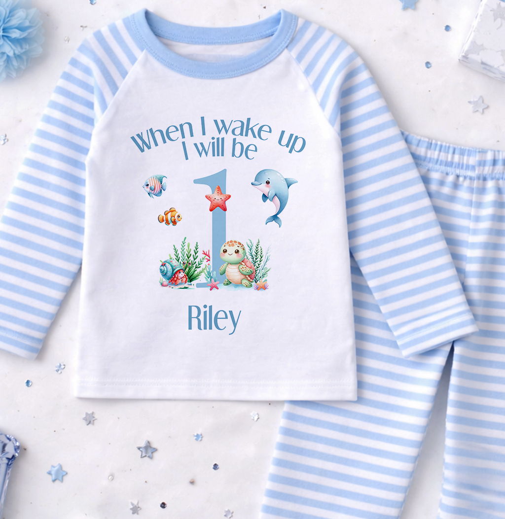 A white and blue striped pajama set with a personalized text and illustrations on the front, along with a blue pom pom and some small star-shaped decorations.