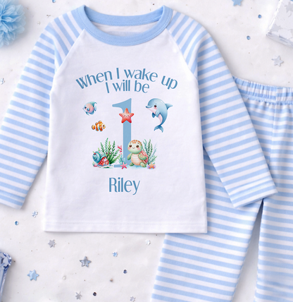 A white and blue striped pajama set with a personalized text and illustrations on the front, along with a blue pom pom and some small star-shaped decorations.