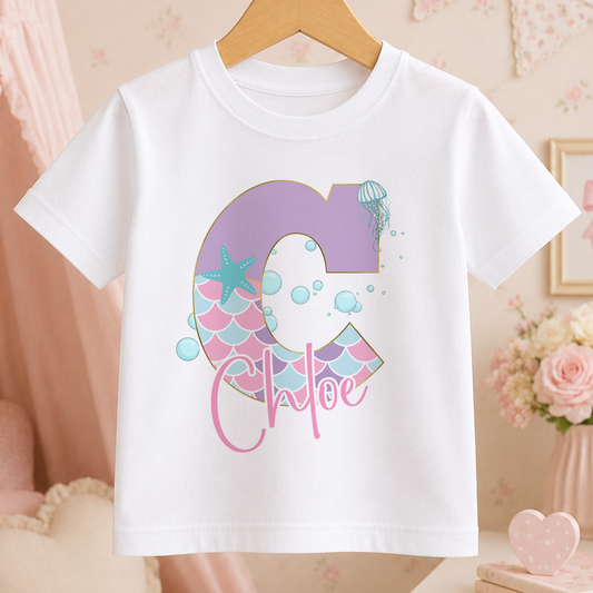A white t-shirt with a personalized name printed on it, featuring a letter 'C' with a mermaid design and bubbles.