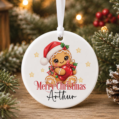Personalised white ceramic Christmas bauble with a gingerbread man in a Santa hat, “Merry Christmas” and a name, hanging on a tree