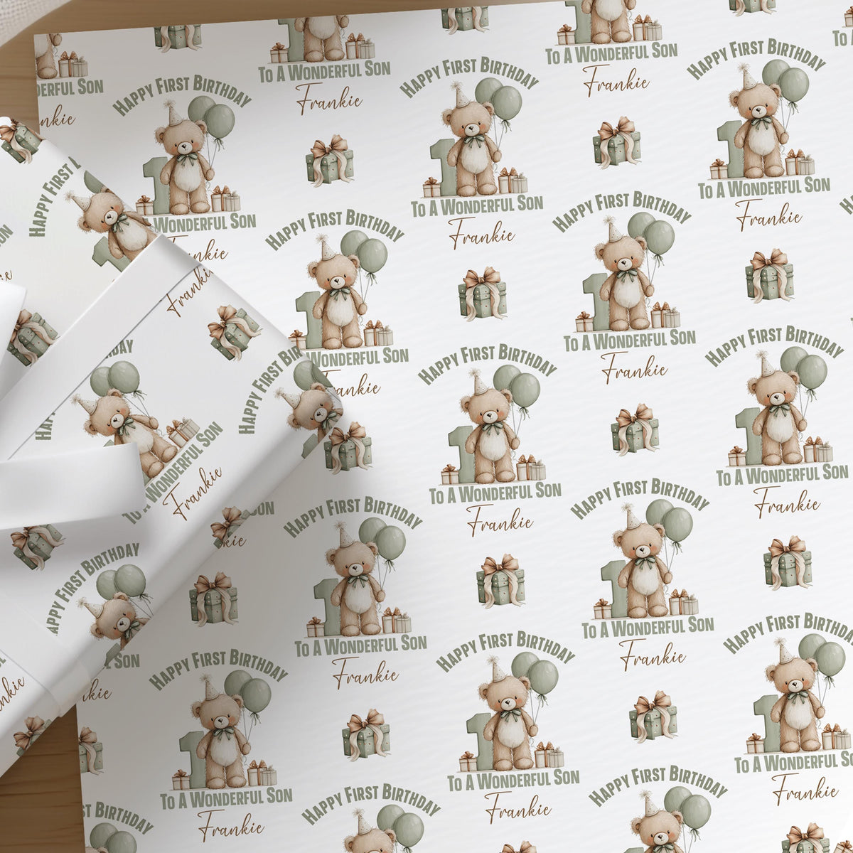 Close-up of personalised teddy bear first birthday wrapping paper for a son, showing the custom printed name among green balloons.
