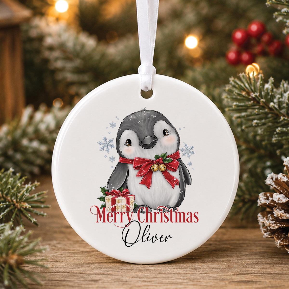 Personalised white ceramic Christmas bauble with a penguin in a red bow holding a present, “Merry Christmas” and a name