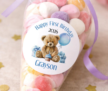 Glossy round stickers featuring a blue teddy bear first birthday design, personalised with the child's name and age.