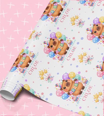 Personalised birthday wrapping paper roll with capybaras in party hats, bunting, pastel balloons, ribbon-tied stars and the name Chloe with Cappy 6th Birthday