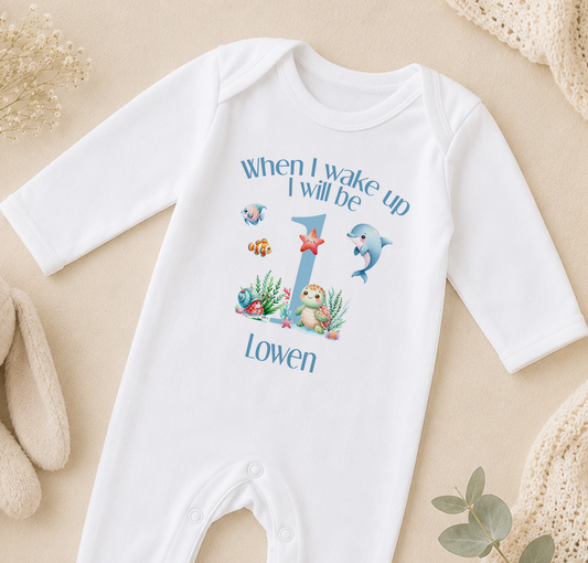 A white onesie with a personalized text and illustrations on it, placed on a beige surface.