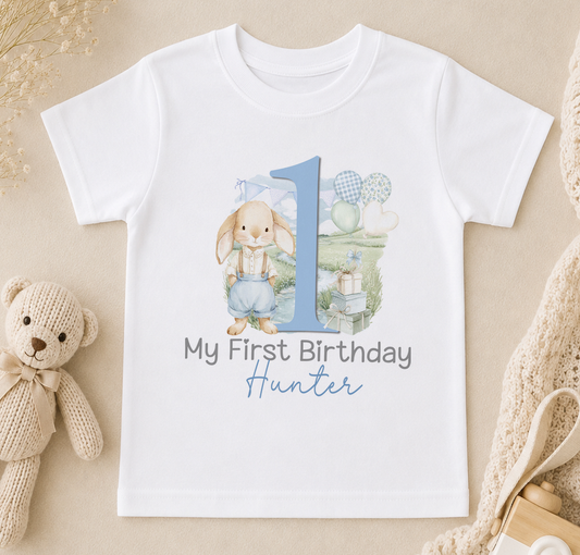 White t-shirt printed with a bunny design, a blue number one and 'My First Birthday' with a personalised name underneath.