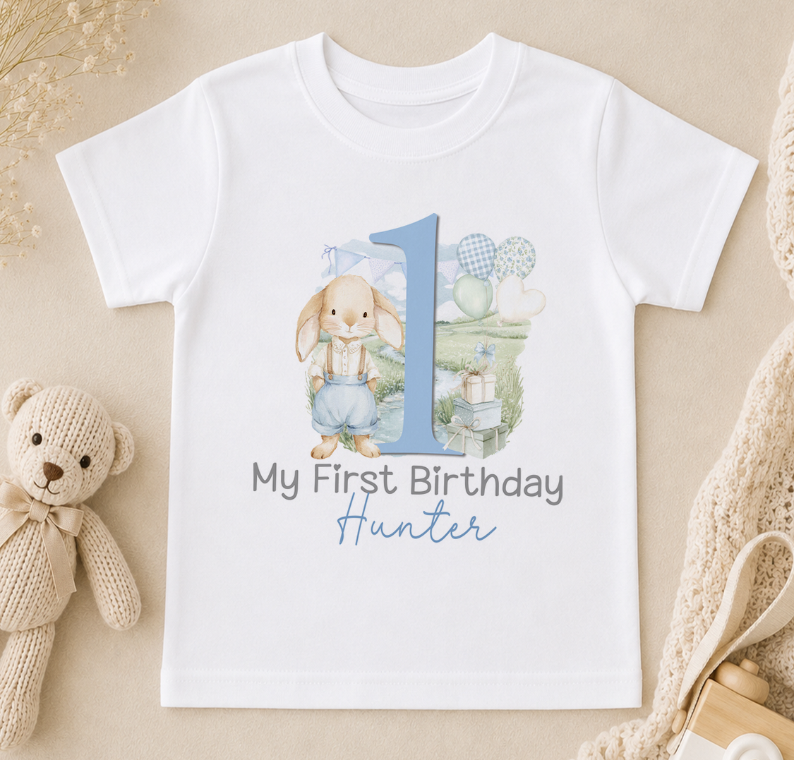 A white t-shirt with a printed design featuring a rabbit and the number 1, along with the text "My First Birthday Hunter".