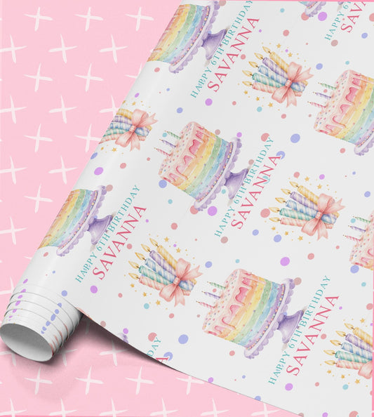 Birthday wrapping paper printed with pastel rainbow layer cakes, bundles of striped candles and confetti dots, with Happy 6th Birthday and the name Savanna on a white background, shown part unrolled