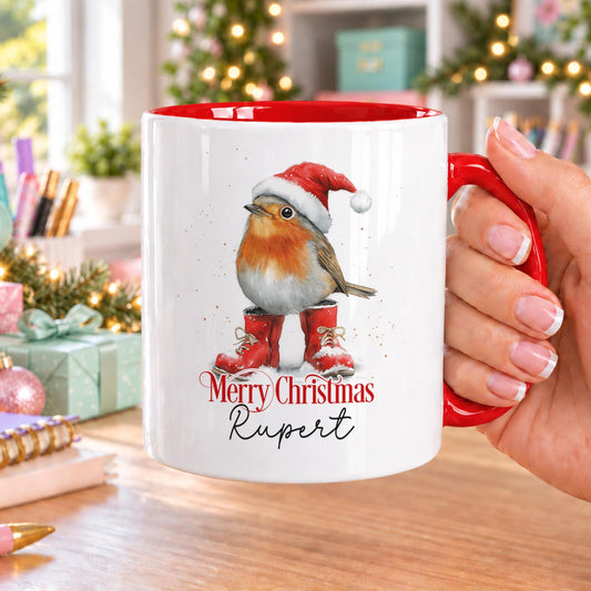 Personalised Christmas robin mug with red handle and inside, showing a robin in a Santa hat and red wellies with Merry Christmas and a name in script