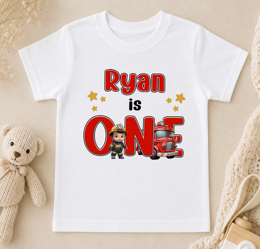 A white t-shirt with a graphic design featuring a firefighter character and the text "Ryan is ONE" along with a red fire truck.