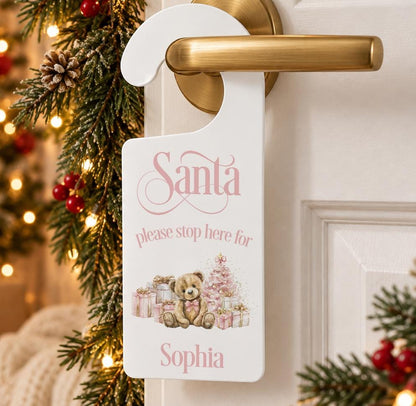 Personalised Santa please stop here door hanger with a teddy bear, pink presents and child’s name, hanging on a door handle