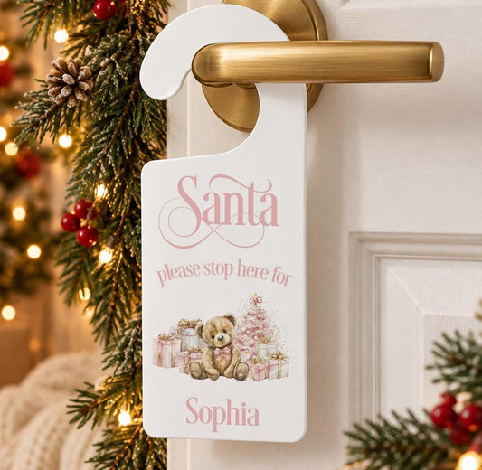 Personalised Santa please stop here door hanger with a teddy bear, pink presents and child’s name, hanging on a door handle