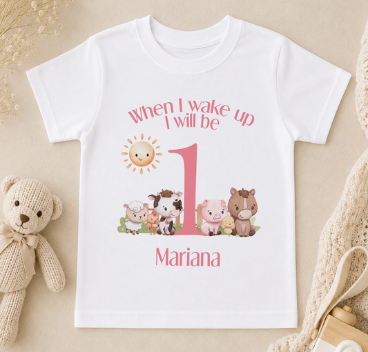A white t-shirt with a personalized design featuring a cartoon image of farm animals and the text "When I wake up I will be 1" along with the name "Mariana".