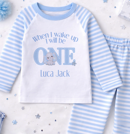 A white and blue pajama set with a personalized text and an elephant graphic, along with some confetti and a blue flower.