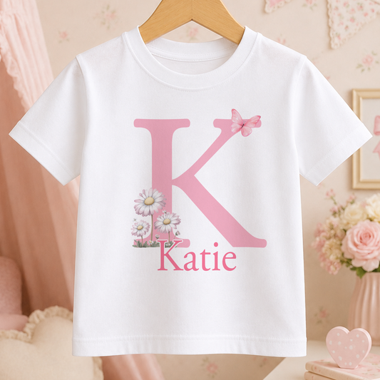 A white t-shirt with a pink letter "K" and a pink flower design, along with the name "Katie" printed below it.