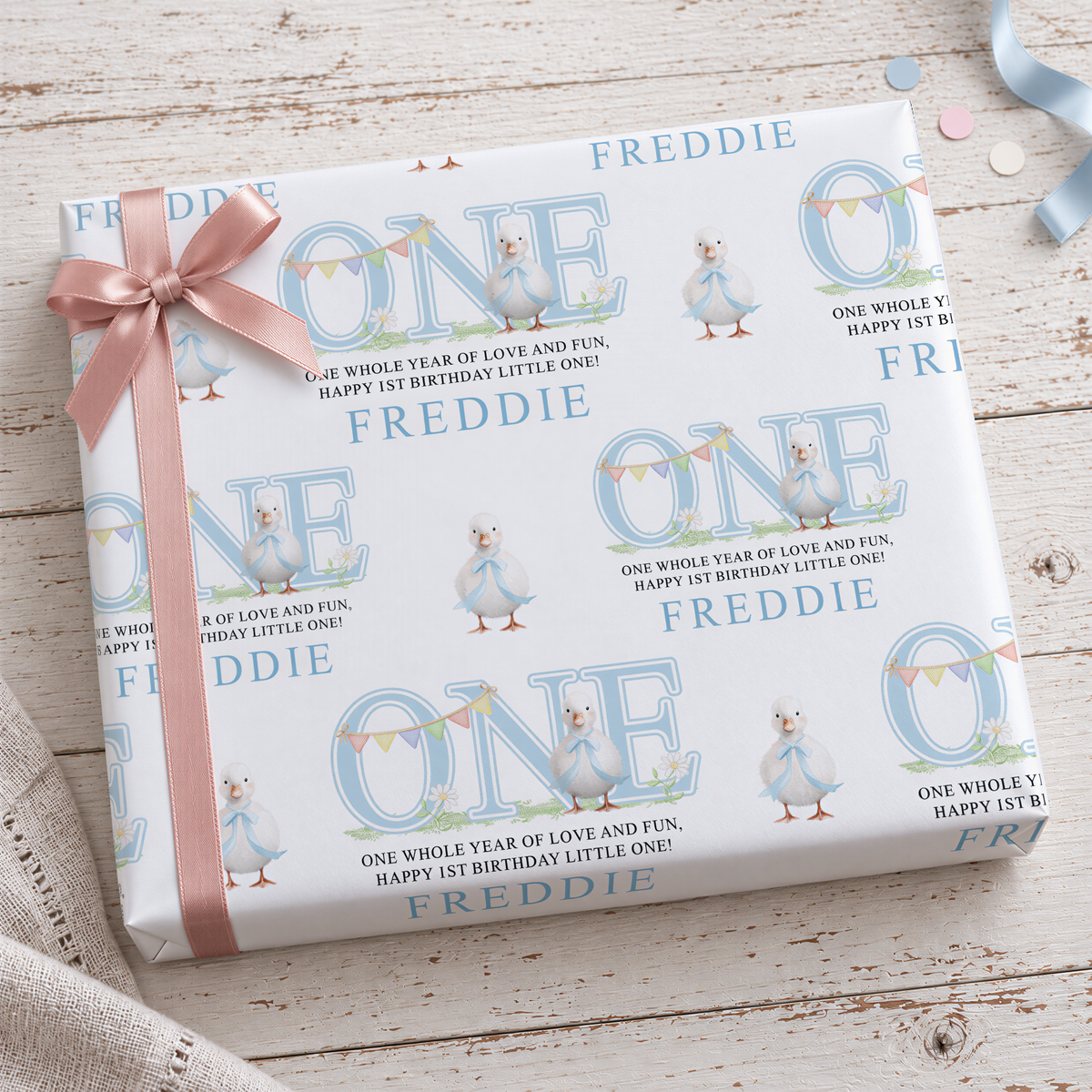 a gift box with a pink ribbon and a repeating pattern of the word "FREDDIE" on it.