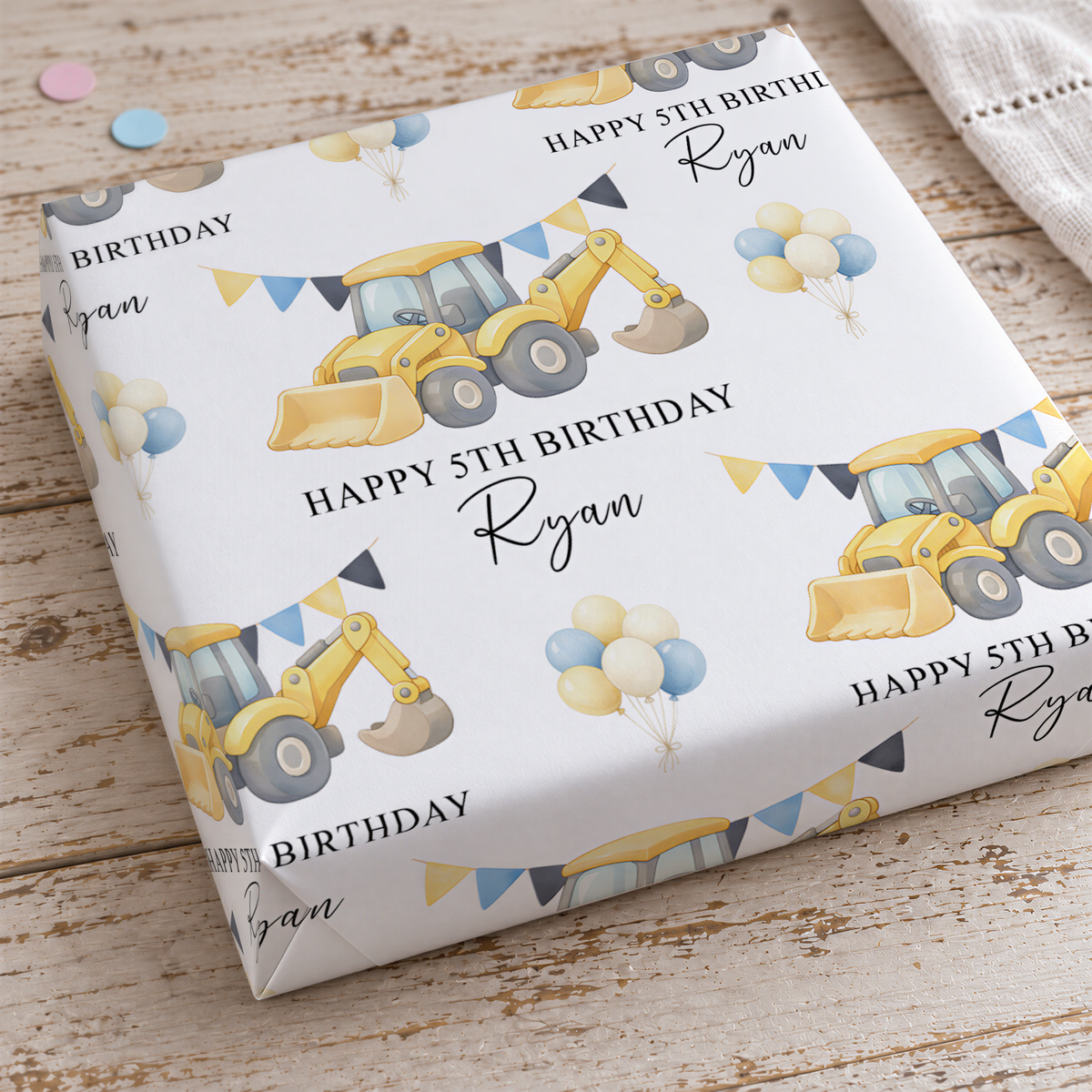 a birthday gift wrapped in a white paper with a repeating pattern of construction vehicles and balloons.