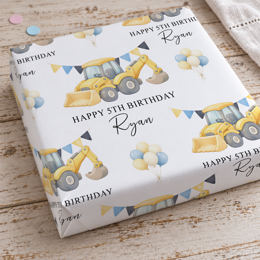 a birthday gift wrapped in a white paper with a repeating pattern of construction vehicles and balloons.