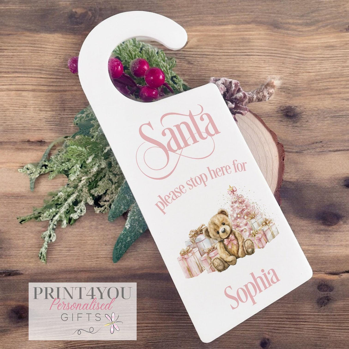 Personalised pink teddy bear Santa Stop Here door hanger laid flat with festive greenery