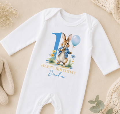 White baby onesie printed with a bunny holding a blue balloon and the message Happy Birthday Jude.