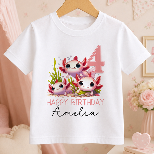 A white t-shirt with a graphic design featuring three cute axolotls, which are a type of salamander, and the text "Happy Birthday Amelia" printed on it.