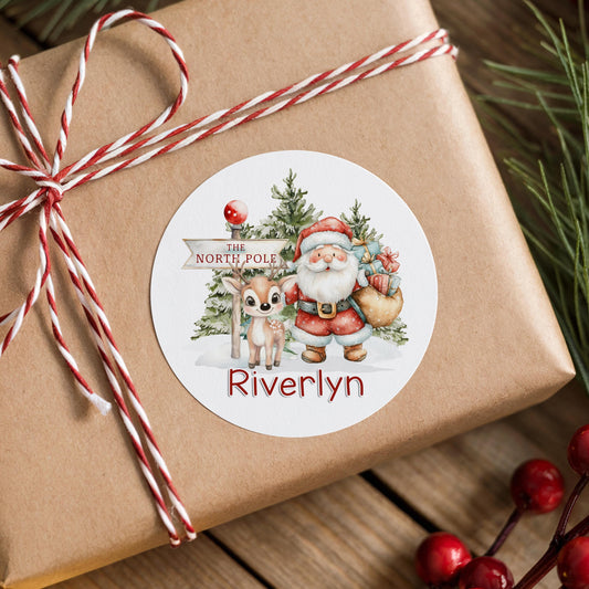 Personalised Santa and reindeer Christmas sticker with a snowy North Pole scene, stuck on a gift box wrapped with twine, printed with a custom name