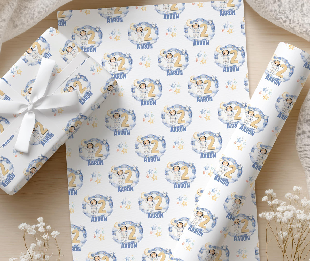 A pair of hands wrapping a gift box in the moon and stars space wrapping paper, finished with white ribbon